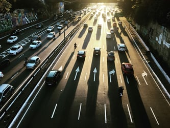 Overhead view of traffic merging from multiple lanes into a single bottleneck, illustrating how AI-accelerated vulnerability discovery shifts the challenge from detection to remediation.